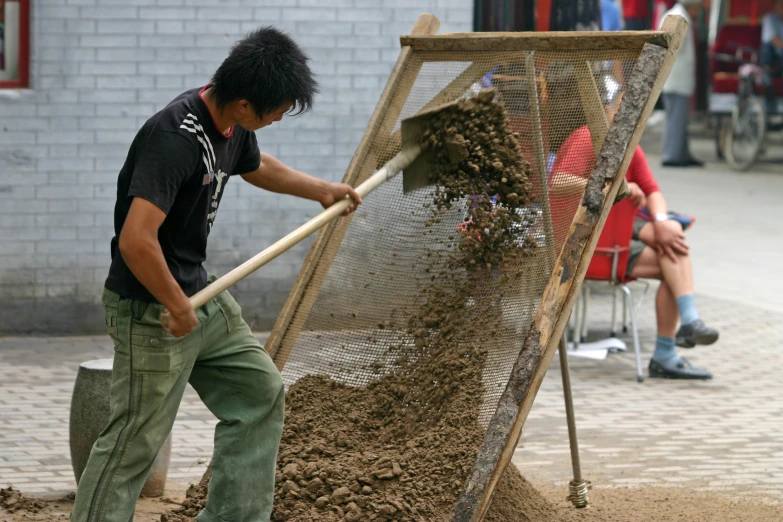 a man shovels dirt outside of a small mesh cage