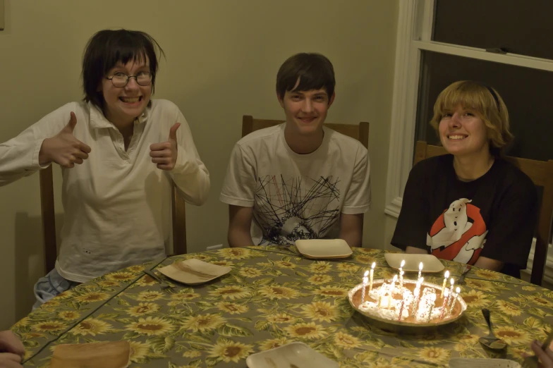 two young people sit next to each other, giving thumbs up while the girl is getting ready to blow out her candles