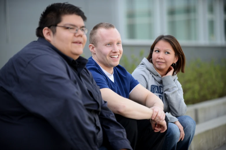 three people sit on a curb smiling and posing