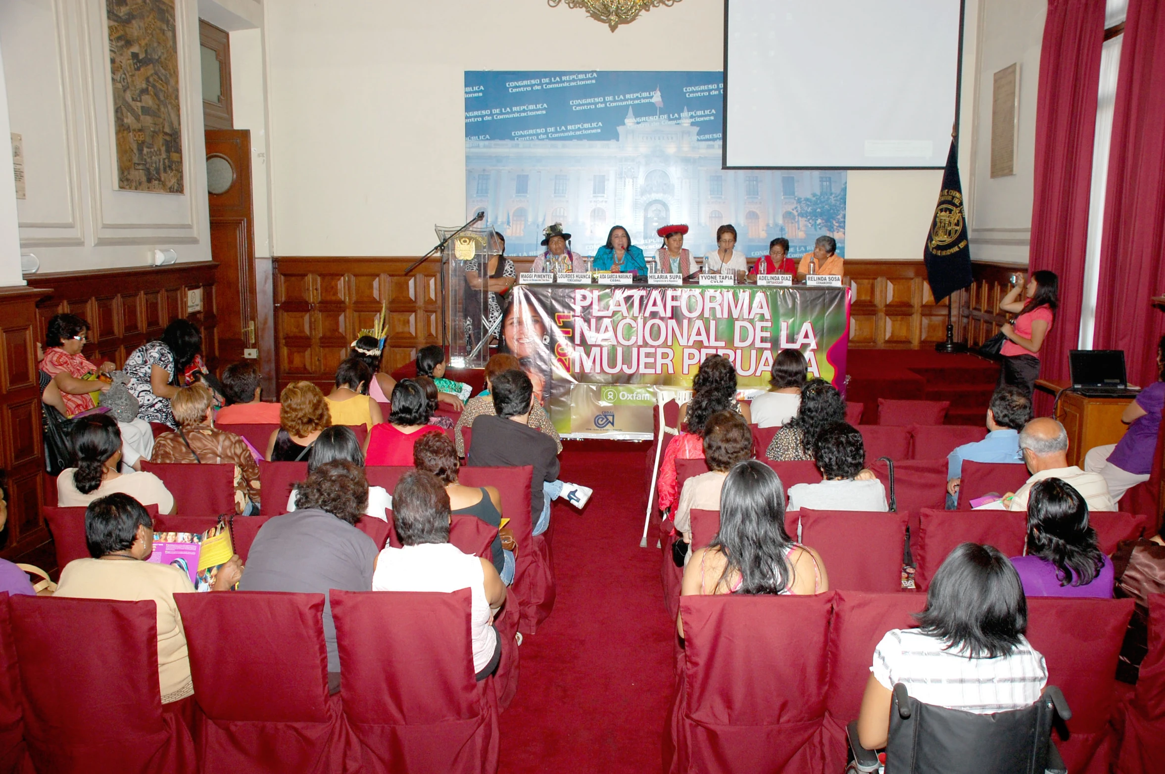 people seated in red chairs and a panel is seen behind them