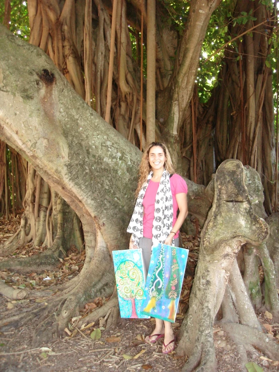 a woman is standing by a tree holding onto three colorful bags