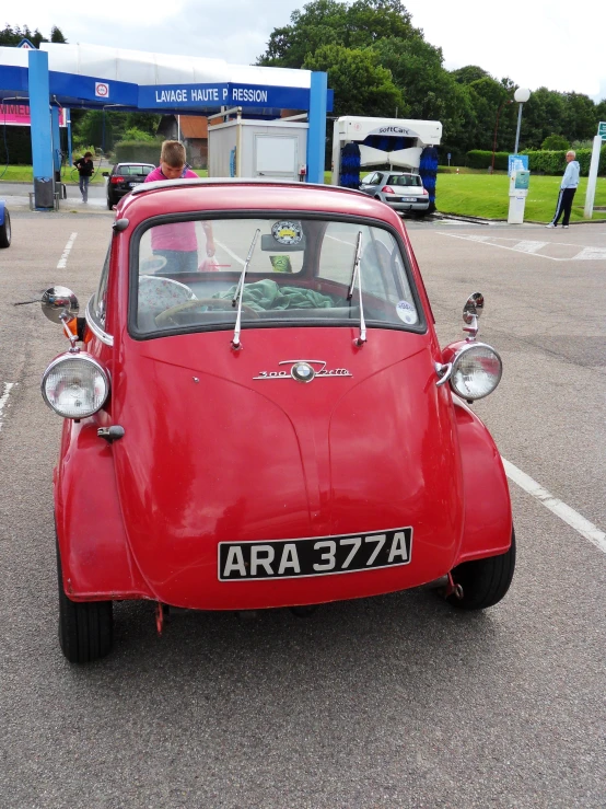 a red car in a parking lot with a blue fuel pump