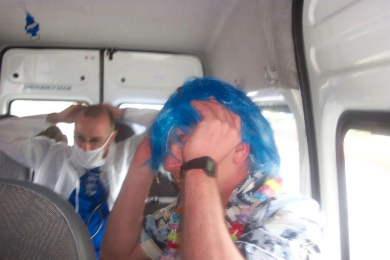 a man with blue hair wearing a mask riding in a vehicle