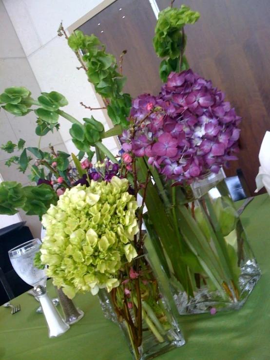 three vases holding different flowers and greens on a table