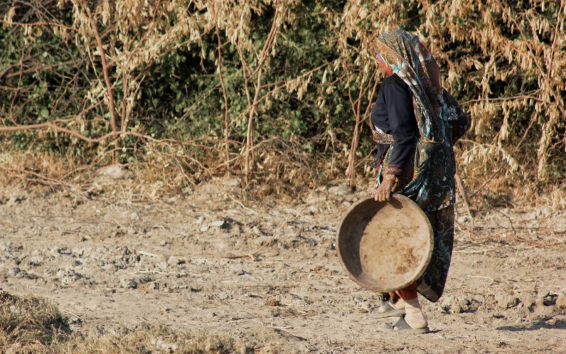 a woman carrying a large drum on a dirt ground