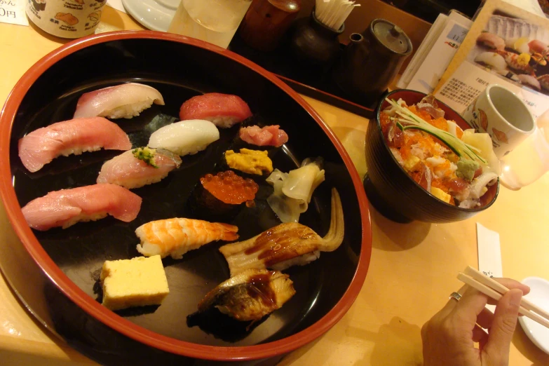 a black bowl filled with assorted sushi next to a plate of rice