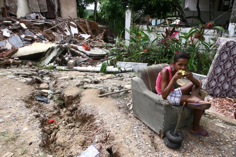 a girl eats an apple on the porch of a destroyed house