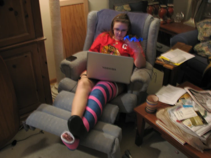 woman in pink shirt on blue reclining chair holding laptop