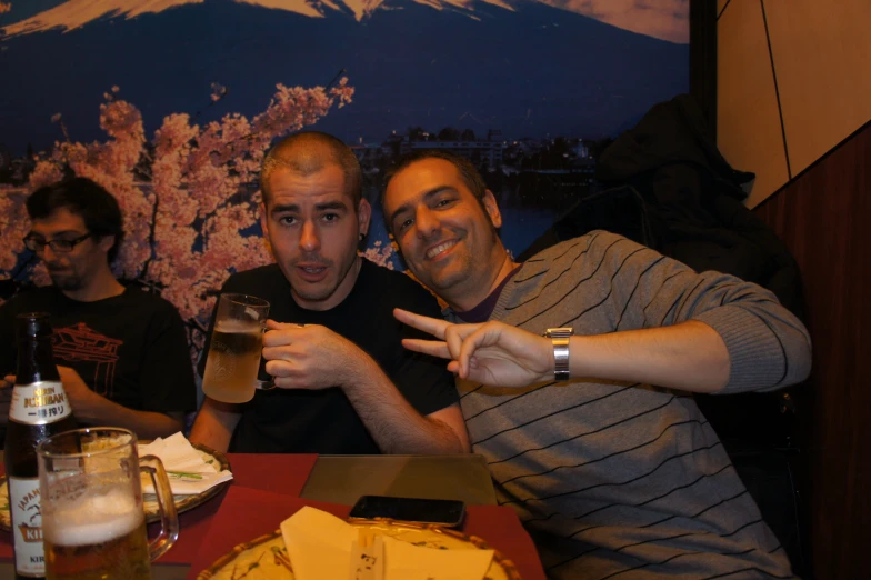 two men pointing at the camera at a table with cheese on it