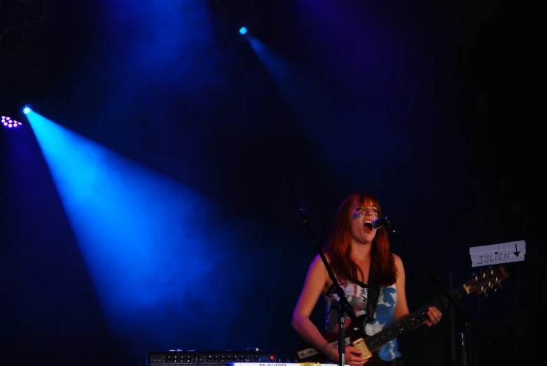 woman with orange hair standing on stage playing guitar