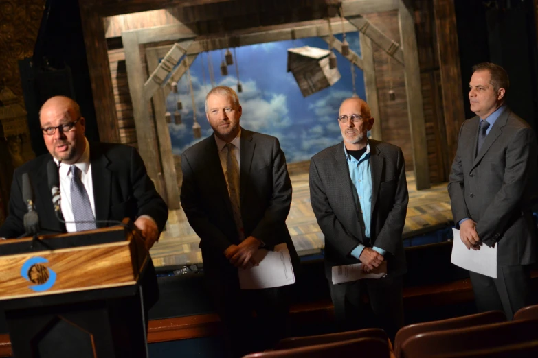 three men stand in front of two podiums, one is speaking