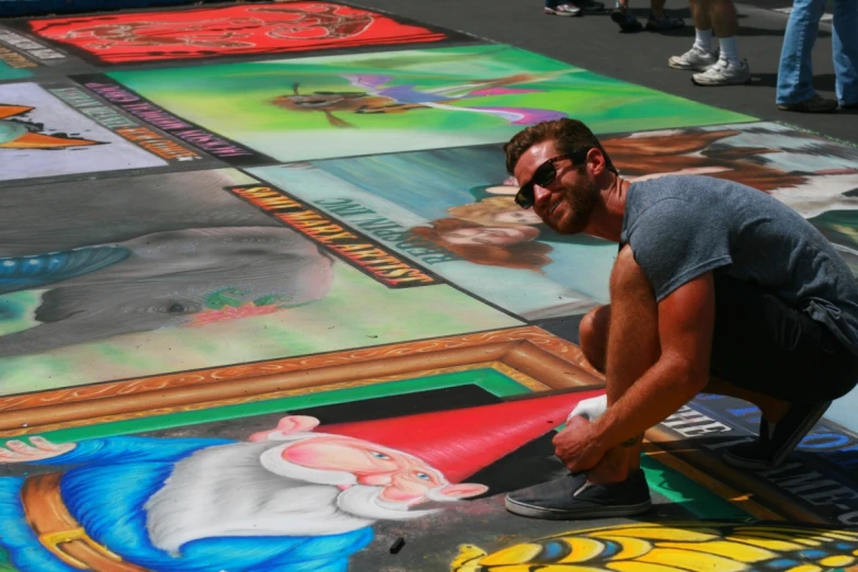 a man in grey shirt kneeling down on pavement with many colored images