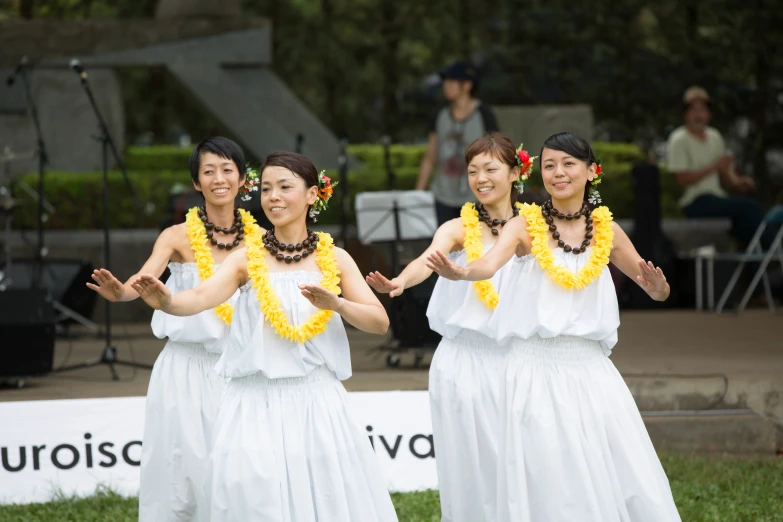 three women in white dresses with yellow flower leis and one wearing a white dress