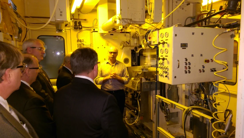 three men stand in front of a huge machine and speak