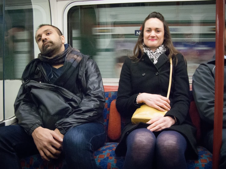 a man and woman sitting on a train, one holding a purse