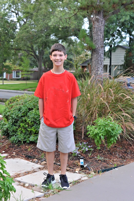 the boy in the red shirt is standing by a tree