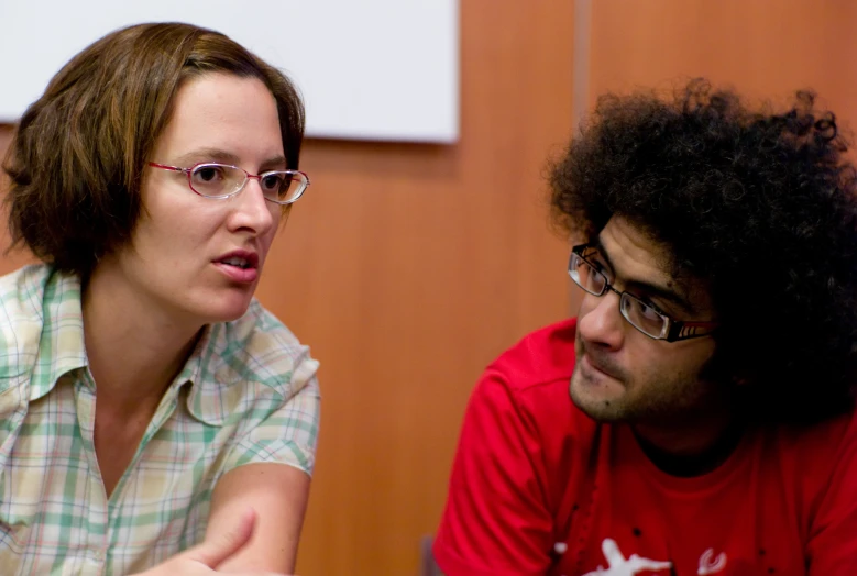 a woman wearing glasses and a man wearing red look toward her