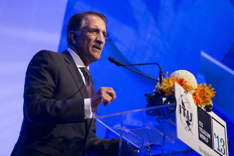 an older man wearing glasses stands at a podium