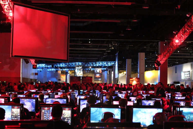 many laptops sitting together at a desk on both sides of the room, and on to the floor, with bright red lighting and black decorations on the walls