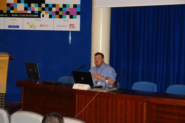 a man sitting in front of a laptop computer while standing next to a podium