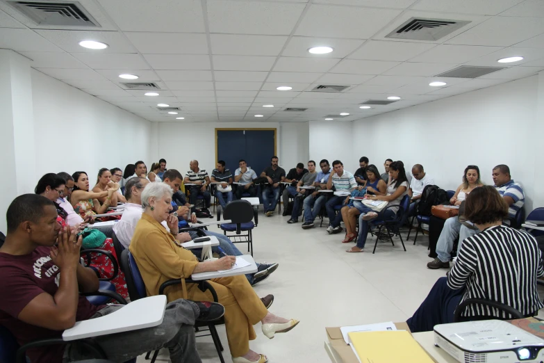 several people are sitting at tables in the classroom listening to a lecture