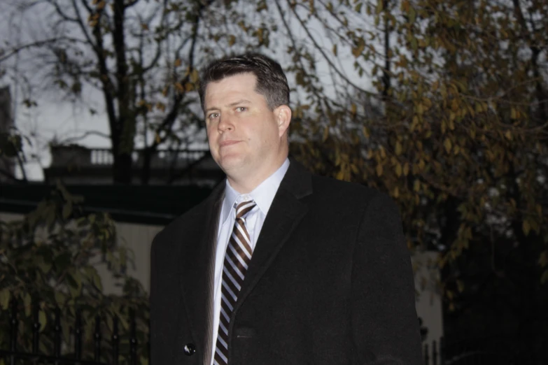 a man in suit and tie standing in front of trees