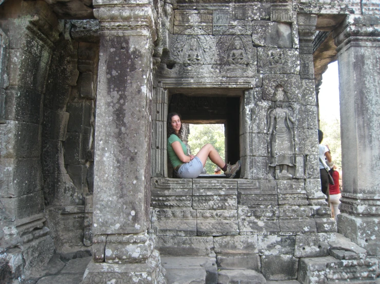 a woman sits in a window above stone structures