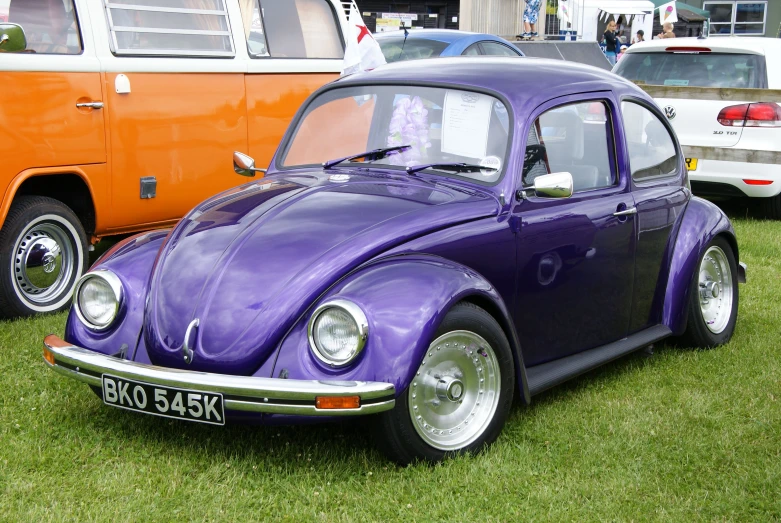 the volkswagen beetle is purple and shiny, and the vw bus is orange