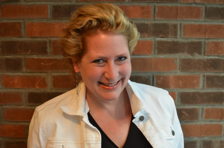 a woman standing by a brick wall smiling