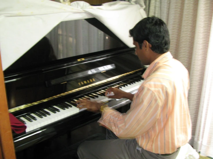 man in striped shirt playing piano in living room