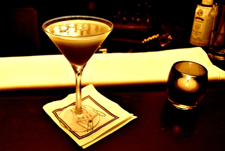 a martini cocktail sitting on top of a table next to an empty glass