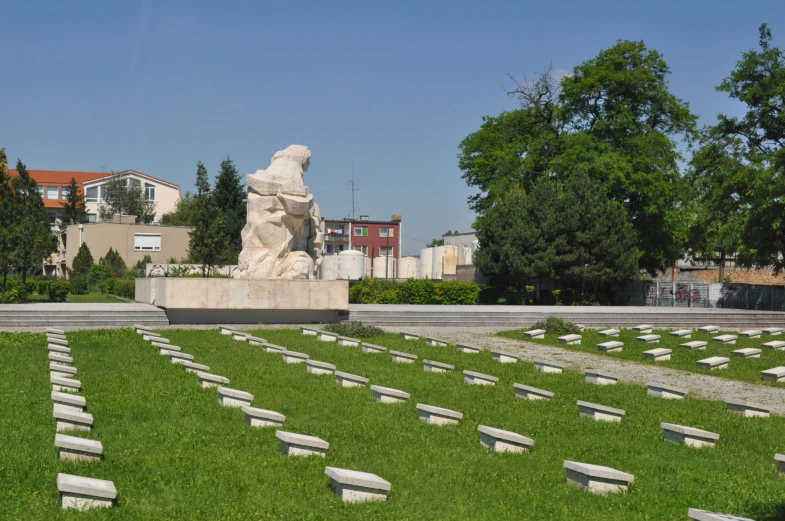 a grassy cemetery has several headstones, a long row of trees and several building in the distance