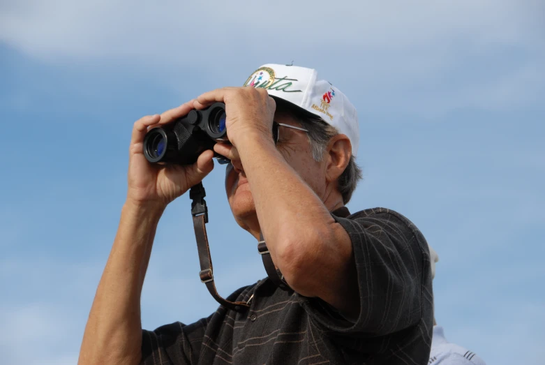 man with cap holding up two large binoculars