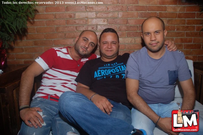 three men sitting together by a brick wall