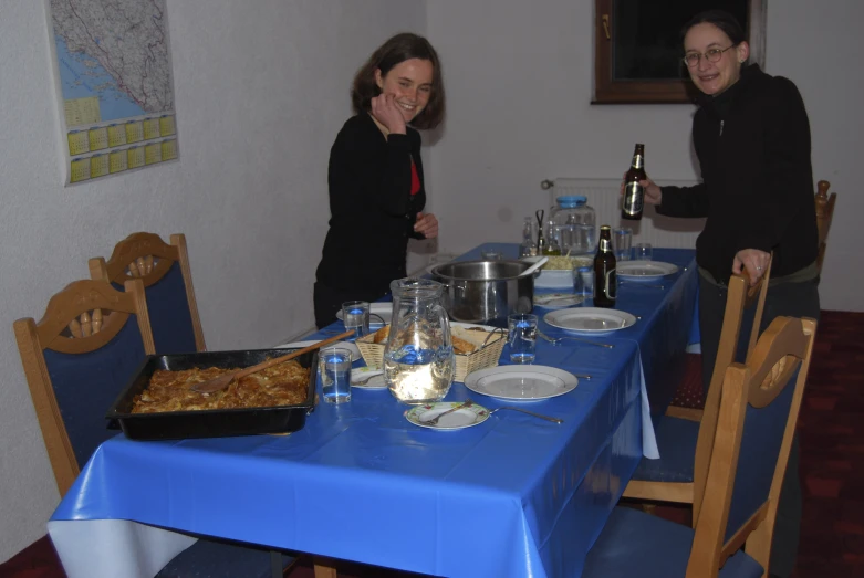 two people standing by a table with a food dish and glasses of wine