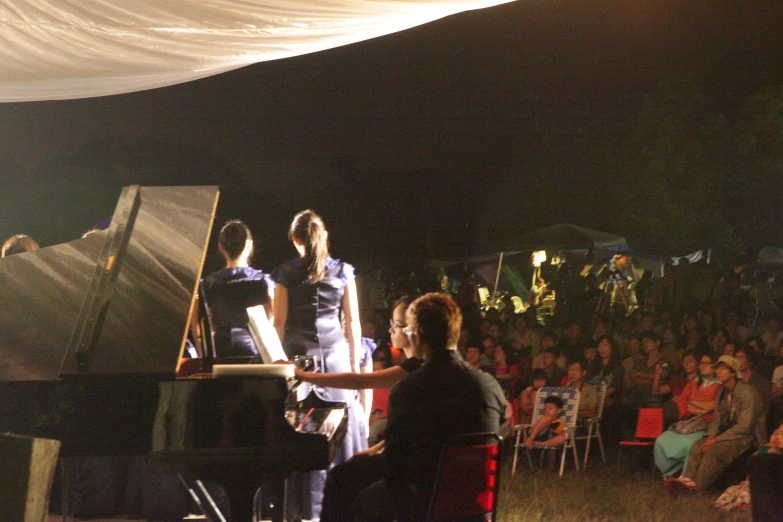 a group of people standing on top of a field next to a piano