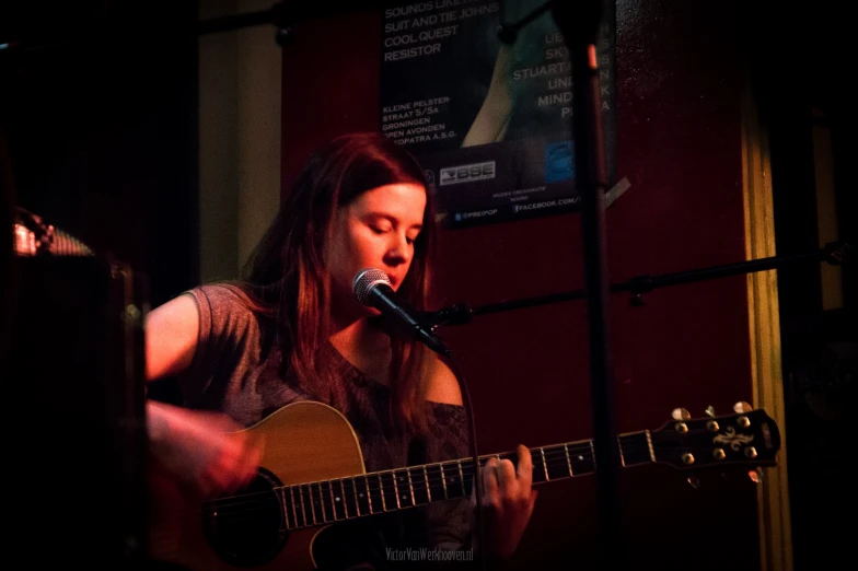 a woman that is playing the guitar at the microphone