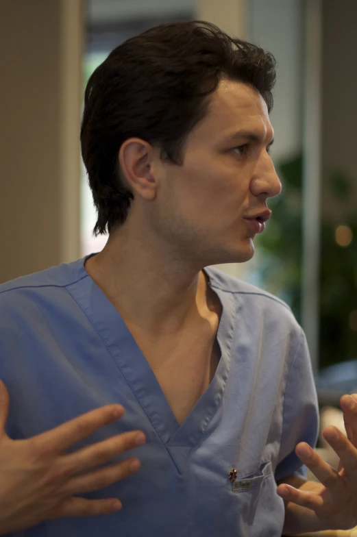 a man in scrubs with an open hand gestures