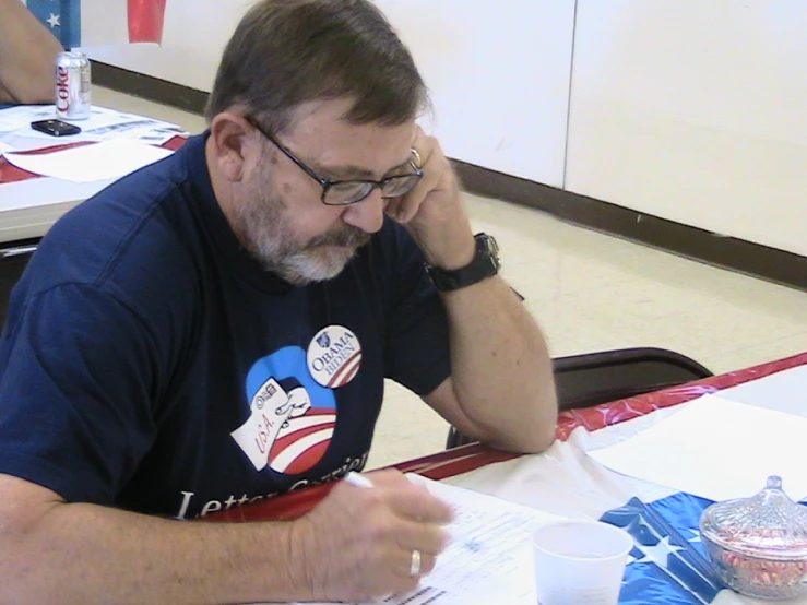 a man in glasses at a table writes with his hand