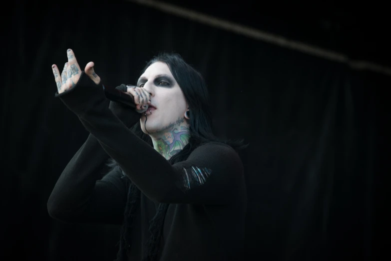 a woman with black and green makeup, piercings on her face, stands against a dark background