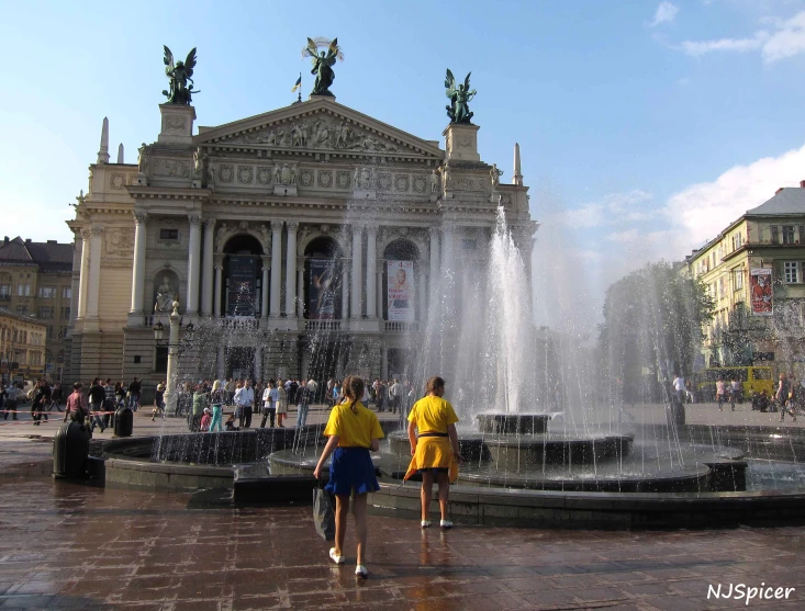 people are walking through a fountain in the middle of a city