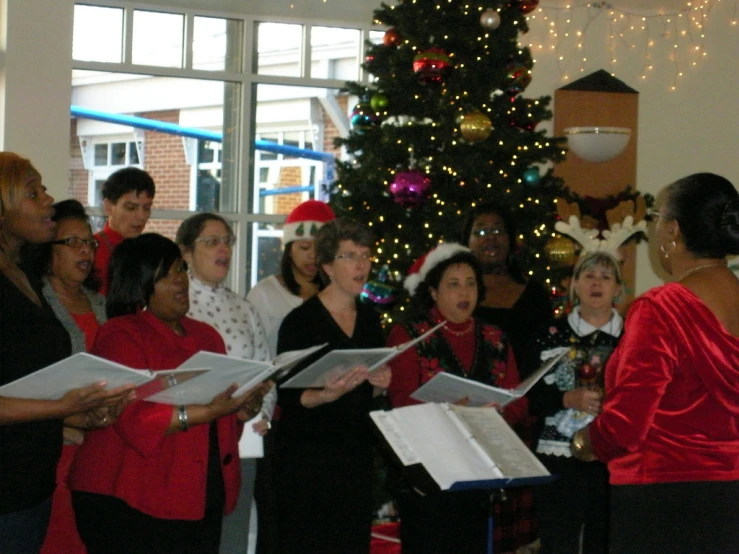 several women with christmas music standing in front of a tree