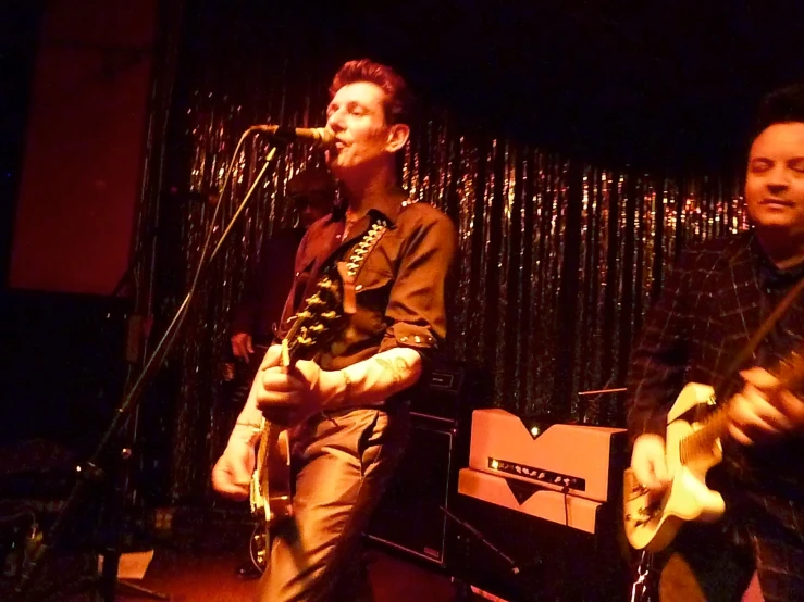 a man singing and playing guitar next to another musician