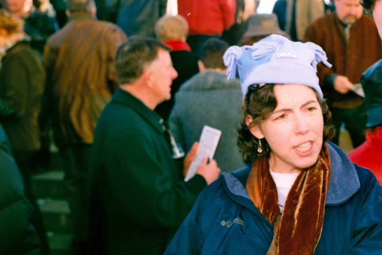 a crowd is standing in line while a woman wearing a blue bonnet smiles