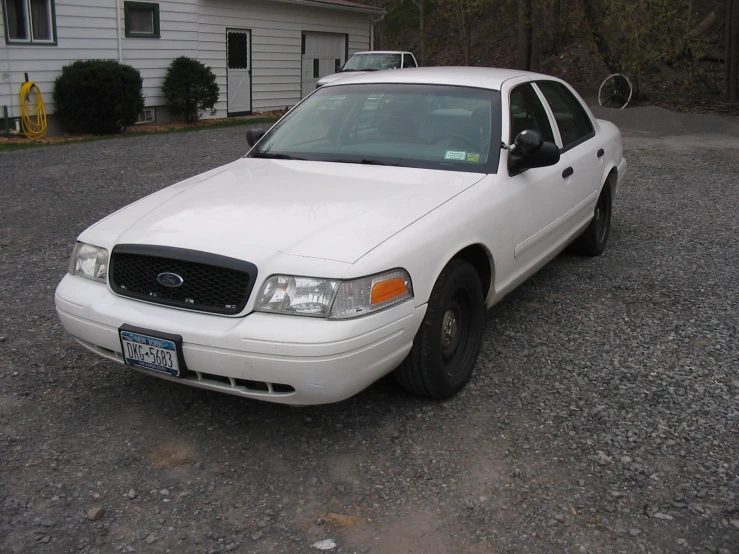 a white ford crown victoria parked in front of a house