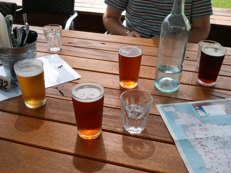 four beers, five glasses and maps on a table outside