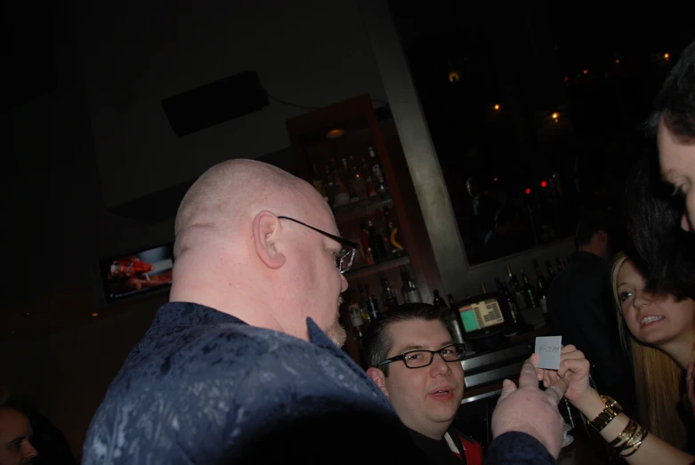 two men standing with one holding up a card at a bar