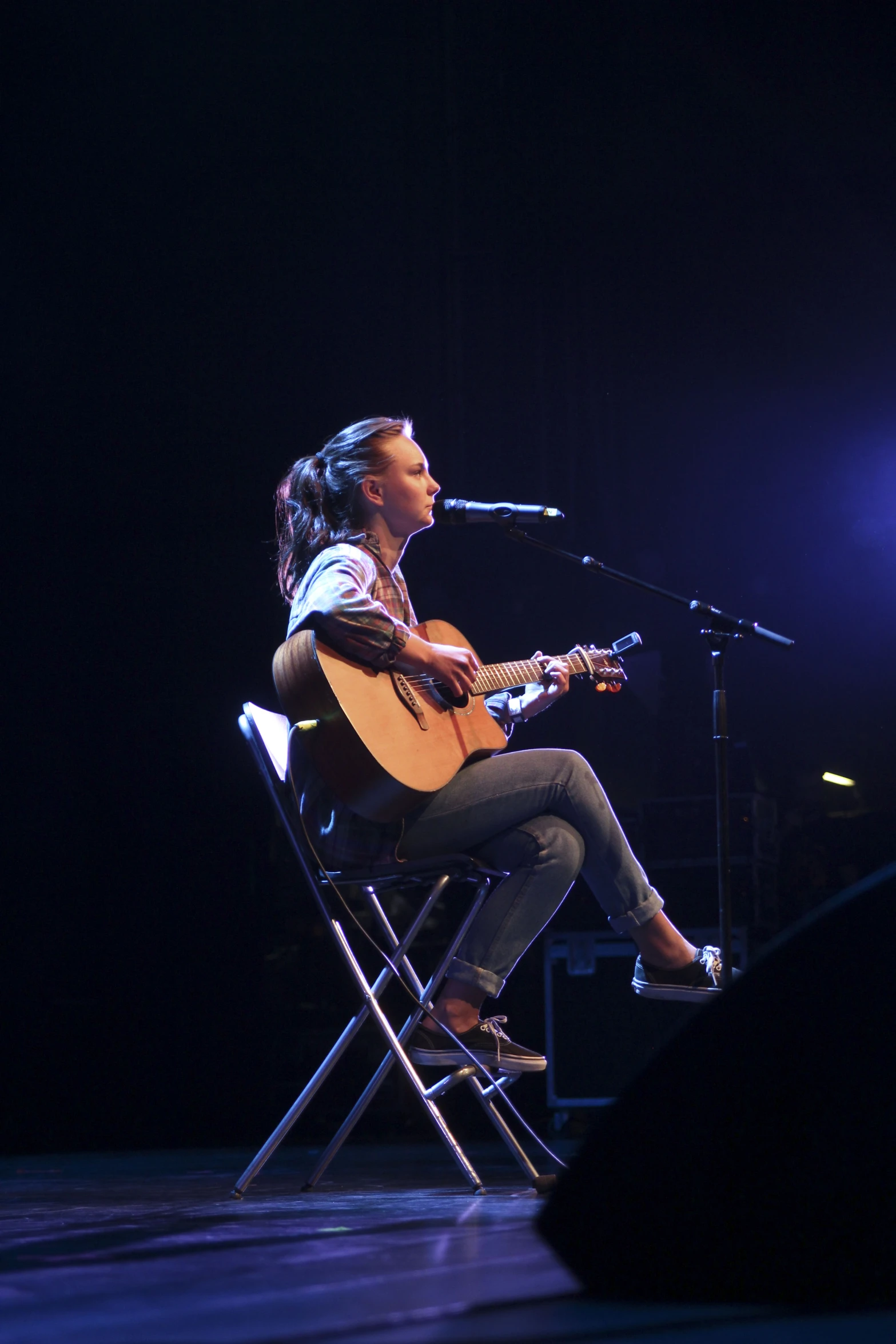 the singer sits on the chair while playing the guitar