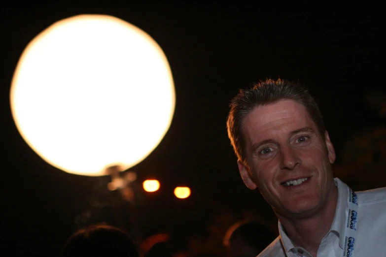 a man in a white shirt stands with his face towards a round light