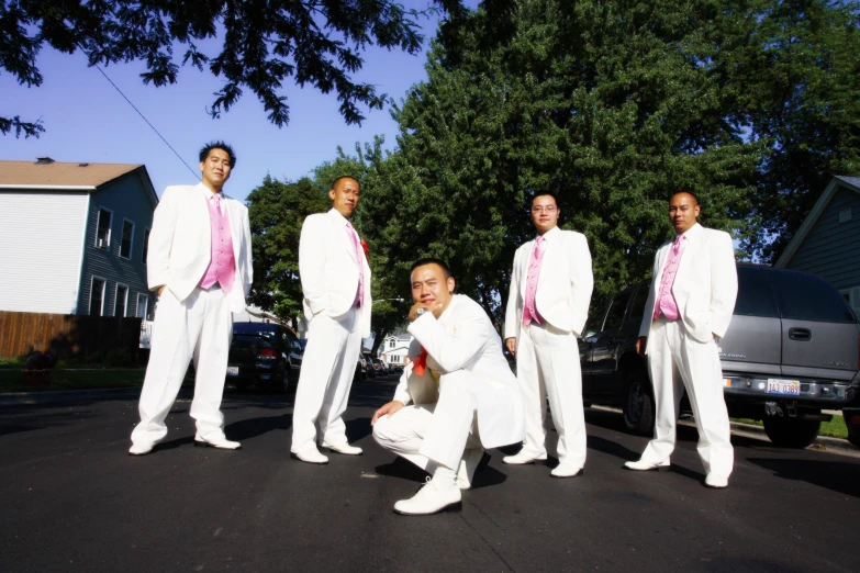 six men in white suit and pink ties are sitting in the middle of a road